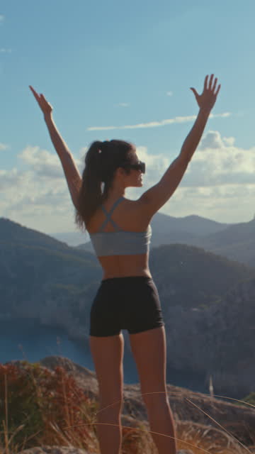 Conquering the mountains. Woman on top of a mountain holding hands up vertical video