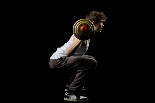 A 17 year old teenage boy wearing a white tank top excercising with a barbell