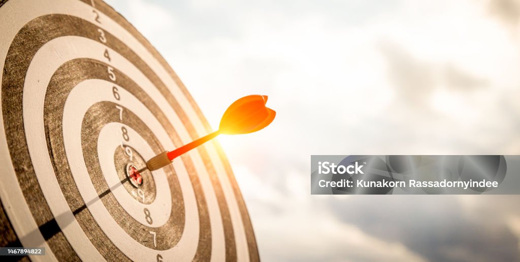 Close up shot red darts arrows in the target  of dartboard center on dark blue sky background. Business target or goal success and winner concept. Aspirations Stock Photo