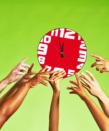 Group of people with arms outstretched towards a red clock, on a green background with copy space.