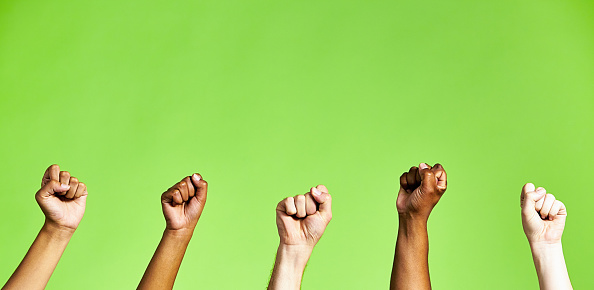 Group of people with raised fists on a green background with copy space.