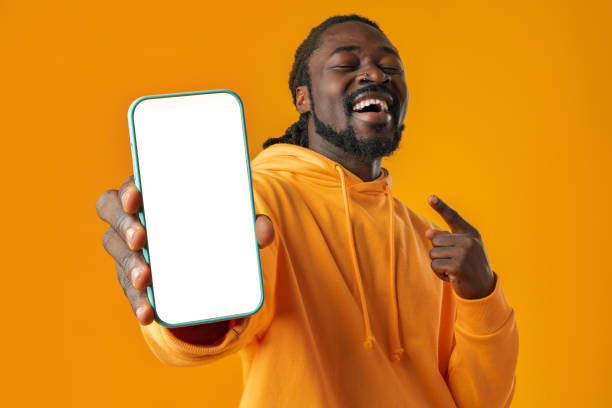 istock Smiling african man pointing at cellphone with blank screen with copy space 1467900930