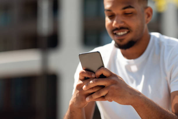 istock Closeup shot of african american man using cellphone, texting or surfing internet, sitting outdoors, focus on device 1467904708