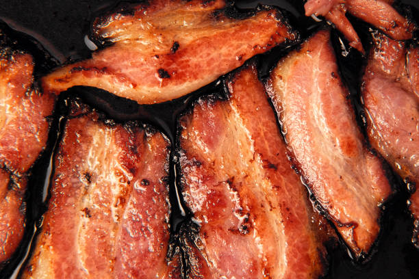 Frying Bacon Slices sizzling in a Pan. Crispy Pieces of Delicious Red Thin Smokey Bacon Fried in a Hot Skillet. Traditional Breakfast. Smoked Bacon Rasher or Strip Being Cooked. Grill. Fat High Calorie Food. freír rodajas de tocino en una sartén. trozos crujientes de delicioso tocino rojo fino ahumado frito en una sartén caliente. desayuno tradicional. rasher de tocino ahumado o tira que se está cocinando. parrilla. alimentos altos en calorías con grasa.