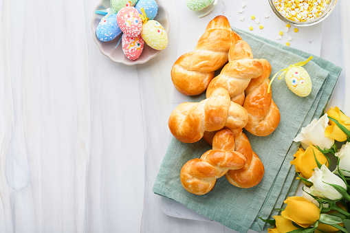 Easter breakfast Holliday concept. Easter bunny buns rolls with cinnamon made from yeast dough with orange glaze, easter decorations, colored eggs on white spring background. Easter Holliday card.