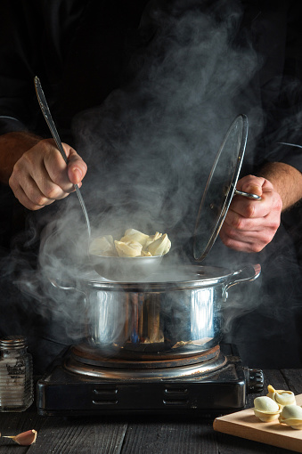 Professional chef prepares pelmeni in a saucepan in the kitchen. Close-up of a cook hands while working