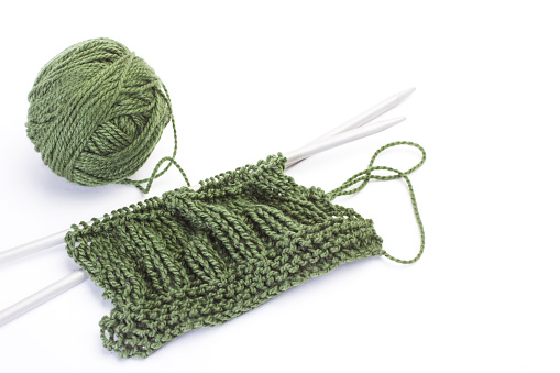 A green ball of wool, knitting needles and a green fabric on a white background with copy space