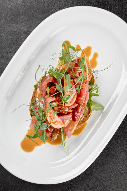 istock Tuna bruschetta on white plate with sauce on black background. Appetizers with crispy bread and sliced tuna fish. Traditional antipasti - fish bruschetta on dark concrete table. Tuna bruschetta. 1467915593