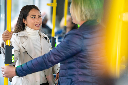 Two female friends talking with each other while standing in bus.