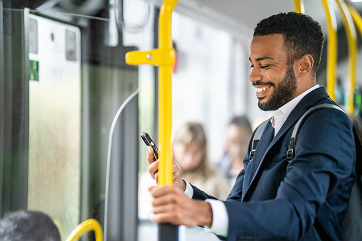 Smiling man using smart phone while standing in bus.