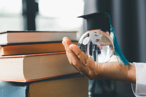 istock Graduate study abroad program concept : Black graduation cap on a globe map and books, depicts knowledge can be learned online anywhere and everywhere, even in universities or campus around the world. 1467917235