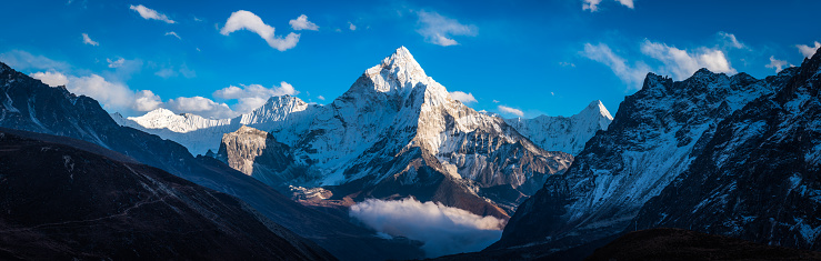 White fluffy clouds in blue high altitude skies over the snow capped peak of Ama Dablam, deep in the Himalayan mountain wilderness of the Everest National Park, Nepal.