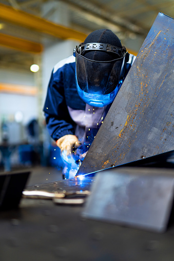 A male welder working in a shop welding steel for a manufacturing project.