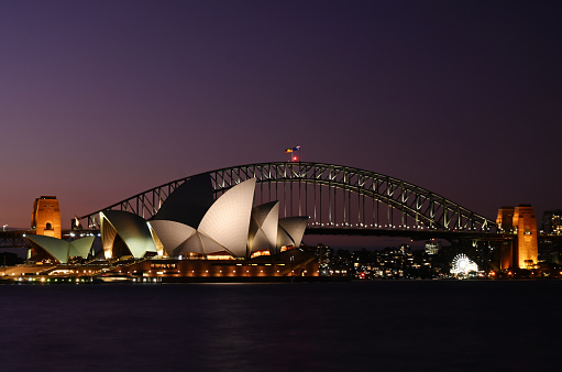 A view across the harbour of Sydney's two most iconic landmarks, the Opera House and Harbour Bridge, with the final glow of the sunset behind.