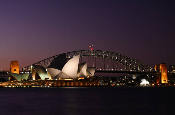 Sydney Harbour at Dusk A view across the harbour of Sydney's two most iconic landmarks, the Opera House and Harbour Bridge, with the final glow of the sunset behind. sydney skyline sunset stock pictures, royalty-free photos & images