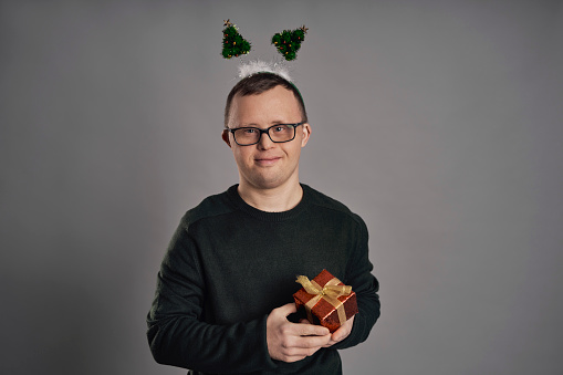 Man with down syndrome holding Christmas present on gray background
