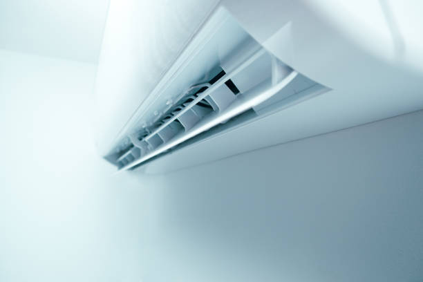 An unrecognizable person holding the remote control in front of the air conditioner at home