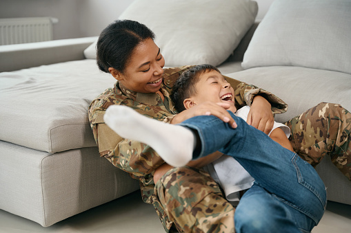 Joyful mom and son have fun playing in the room, a woman in military uniform