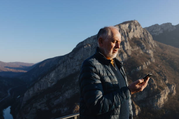 istock Senior man his black smartphone. Behind him is a beautiful landscape 1467930057