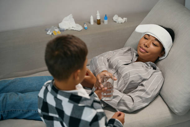 il bambino dà un bicchiere d'acqua a una madre malata - bugiardo su fronte foto e immagini stock