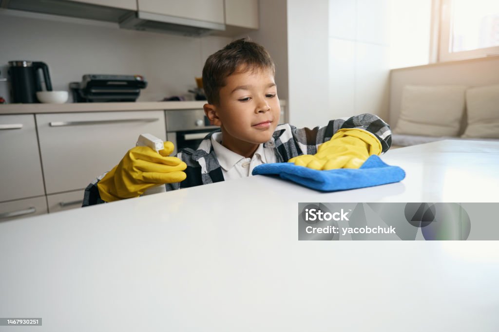 Teenager in plaid shirt and protective gloves helps around house Teenager in a plaid shirt and protective gloves helps around the house, he washes the kitchen surface Child Stock Photo