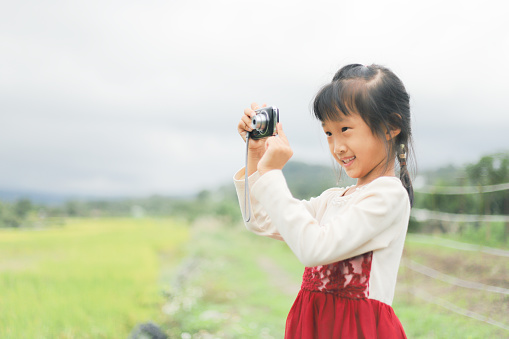 a smiling Asian girl take photos with a digital camera by the field.