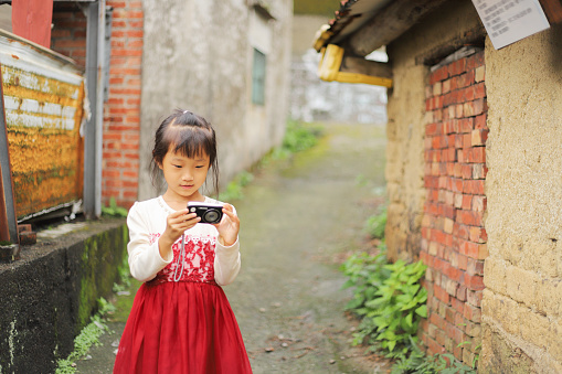 a Asian girl taking pictures in the alley next to the old house