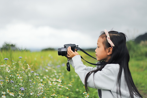 a smiling Asian girl take photos with a digital camera on the meadow.