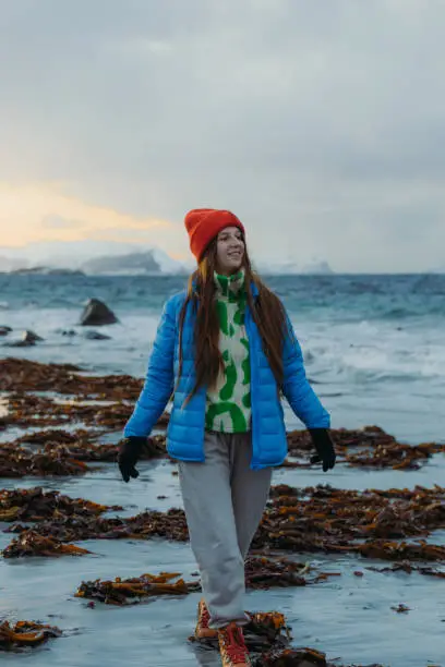 Happy female with long hair and inblue jacket walking at the scenic beach with cold ocean view in Scandinavia