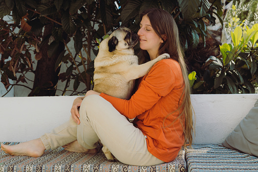 A footage of happy female with long hair in orange shirt lying with a pug at the home terrace playing and having happy time in Turkey