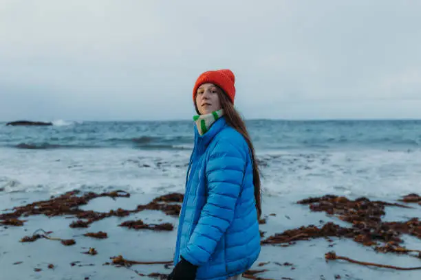 Side view of a female with long hair and inblue jacket walking at the scenic beach with cold ocean view in Scandinavia