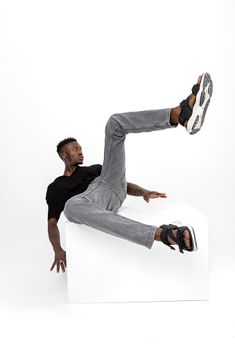 Black handsome man of African descent wearing black shirt, gray jeans, black sports shoe with cubes in studio.