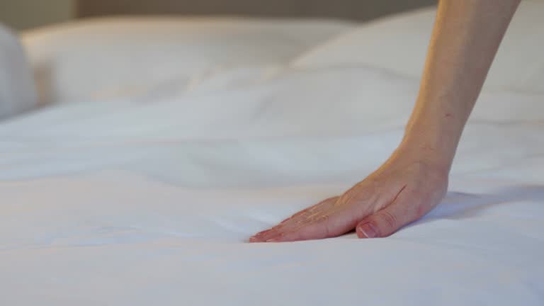 A woman touches the white bed linen on the bed with her hand, close-up