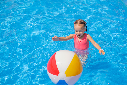 The baby is running after an inflatable ball on the water in the pool.  Summer vacation at the sea with children