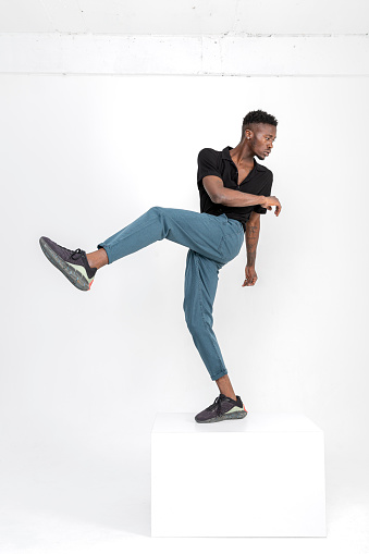 Black handsome man of African descent wearing black shirt, gray fabric pants, black summer sandals with cubes in studio.