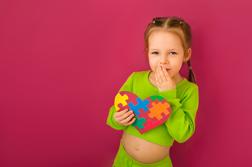 A shy little lady holds an autism symbol as a sign of support for children suffering from autism spectrum syndrome. The child covers his mouth with his hand embarrassed