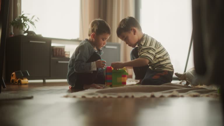 Portrait of Two Male Asian Kids Playing with Colorful Building Blocks in Their Room During the Day. Big Brother Helping Younger Sibling to Construct a Toy House. Concept of Childhood and Innocence