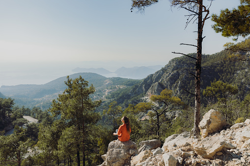 A woman traveler enjoying mountain trip in Mediterranean Turkey and sitting on the viewpoint with dramatic view of raw nature during bright sunset