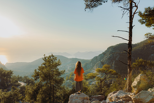 A woman traveler enjoying mountain trip in Mediterranean Turkey and staying on the viewpoint with dramatic view of raw nature during bright sunset