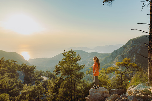 A woman traveler enjoying mountain trip in Mediterranean Turkey and staying on the viewpoint with dramatic view of raw nature during bright sunset