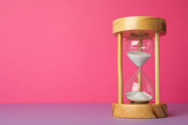 istock Hourglass with flowing sand on violet table against pink background, space for text. Menopause concept 1467942369