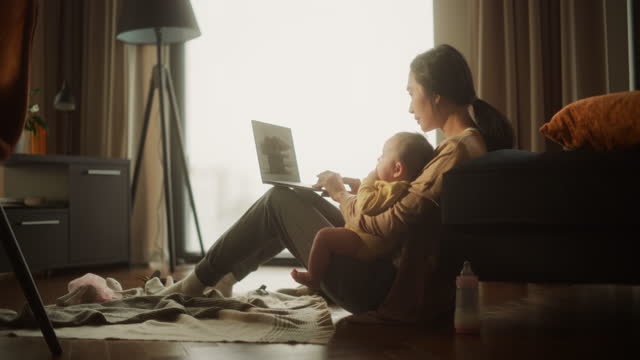 Working from Home: Portrait of Young Asian Mother, Holding her Cute Baby and Working on Laptop Computer During Day. Successful Female Architecte Balancing Life and Work while Doing her Job Remotely