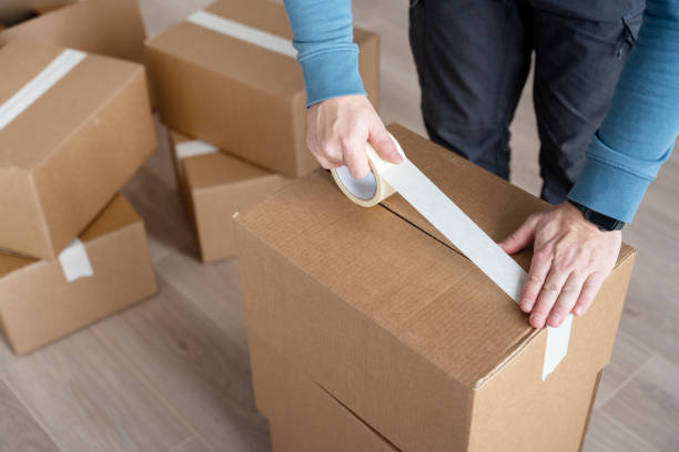 A man uses adhesive tape to packing cardboard box. Moving home concept stock photo