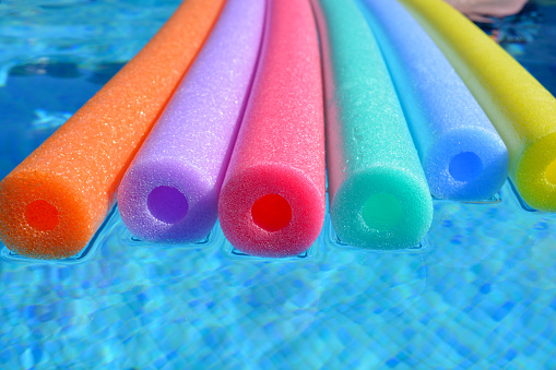 Multi coloured polyethylene hollow swim noodles floating in swimming pool