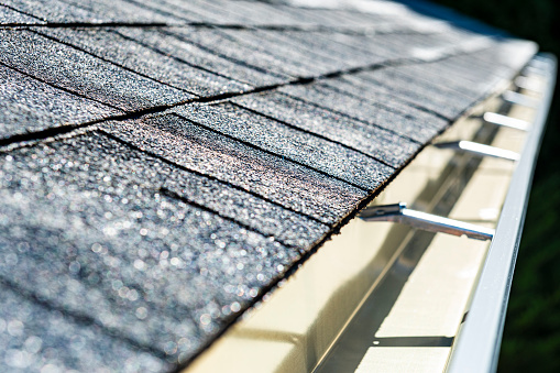 A close-up of a newly installed architectural shingle roof and seamless aluminum rain gutters on a residential home.
