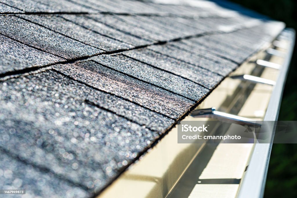 Close-up of a newly installed shingled roof and seamless aluminum rain gutters A close-up of a newly installed architectural shingle roof and seamless aluminum rain gutters on a residential home. Roof Gutter Stock Photo