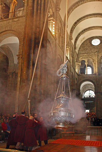 Santiago de Compostela, Spain- March 7, 2010: Group of men moving the Botafumeiro with ropes , famous ancient thurible hanging and swinging from the ceiling of the Santiago de Compostela Cathedral, Galicia, Spain. Group of worshippers in the background, religious mass.