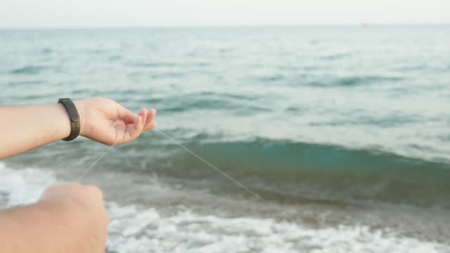 A man's hands pulling a fishing line out of the sea, fishing. Close-up.
