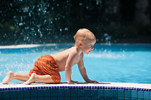Funny photo of active baby splashing in swimming pool with fun, jump deep down underwater. Child learn to swim. Healthy family lifestyle, summer children water sport activity and lessons with parents