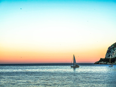 a sailboat in the blue sea and with a summer sunset, in Western Liguria in July 2022